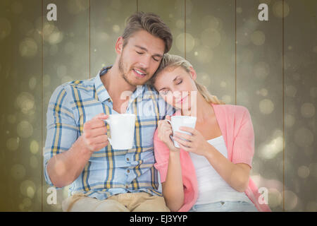 Composite image jeune couple assis holding mugs Banque D'Images