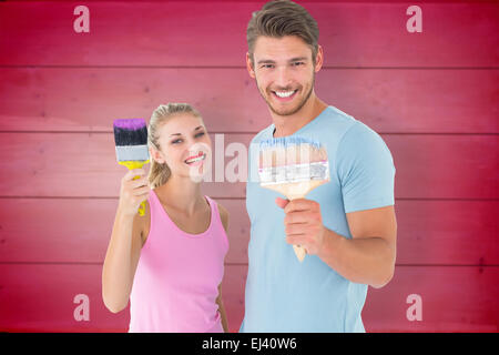 Image composite de young couple smiling and holding paintbrushes Banque D'Images