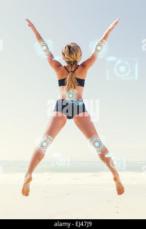 Image composite de fit blonde jumping on the beach with arms outstretched Banque D'Images