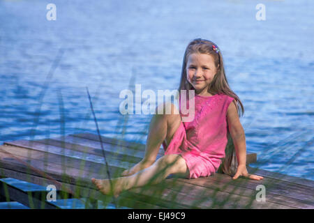 Petite fille assise près du lac en été à l'extérieur Banque D'Images