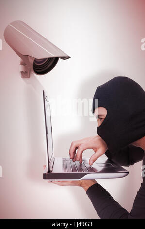 Image composite de l'accent cambrioleur avec balaclava typing on laptop Banque D'Images