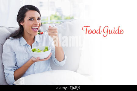 Guide alimentaire contre cheerful woman relaxing on the sofa eating salad Banque D'Images