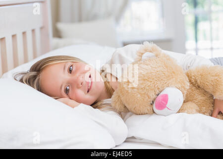 Petite fille couchée dans son lit tenant son ours en peluche Banque D'Images