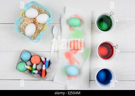 High angle still life shot de Œuf de Pâques mourir,tasses plein de colorant, d'un panier d'oeufs, oeufs teints, et des marqueurs pour la décoration. Banque D'Images