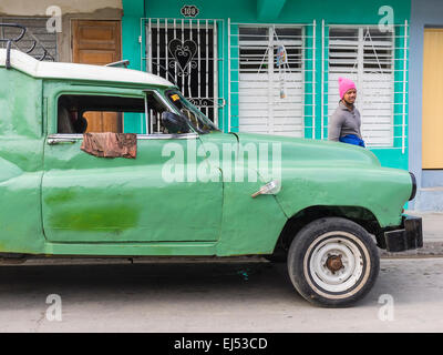 Afro-cubain un homme portant un chapeau en laine rose chaud s'en tient à un livre vert et blanc beat-up vieille voiture à Santiago de Cuba. Banque D'Images