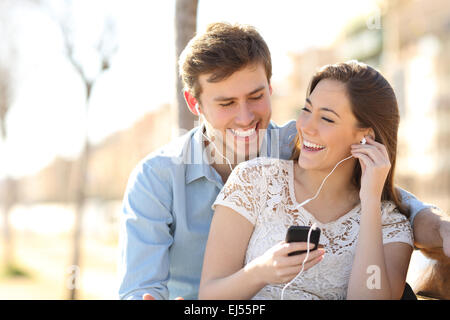 Couple à écouter la musique avec les écouteurs d'un téléphone intelligent dans un parc avec un milieu urbain Banque D'Images