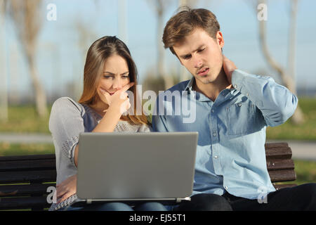 Les étudiants entrepreneurs inquiets ou regarder un ordinateur portable assis sur un banc dans un parc Banque D'Images