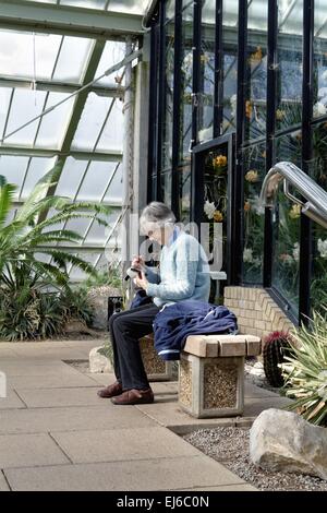 Personnes âgées seule dame à l'aide de téléphone mobile dans une serre de Kew Banque D'Images