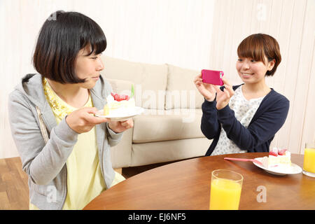 Les jeunes filles japonaises ayant un morceau de gâteau ensemble dans la salle de séjour Banque D'Images