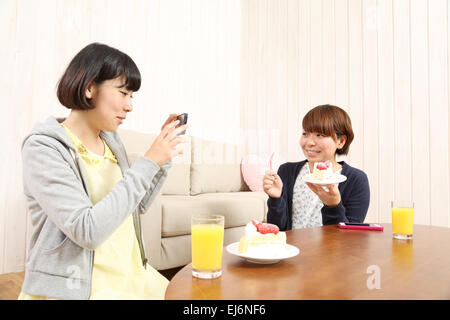 Les jeunes filles japonaises ayant un morceau de gâteau ensemble dans la salle de séjour Banque D'Images