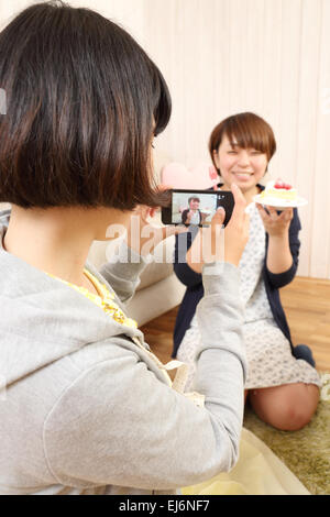 Les jeunes filles japonaises ayant un morceau de gâteau ensemble dans la salle de séjour Banque D'Images