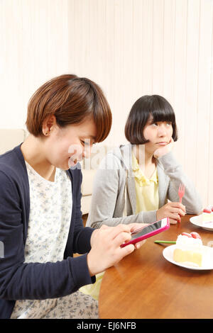 Les jeunes filles japonaises ayant un morceau de gâteau ensemble dans la salle de séjour Banque D'Images