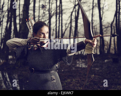 Archer médiéval femme, elle porte une maille et utiliser un arc et une flèche, forêt sombre, contre-image traitée. Banque D'Images