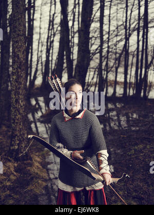 Archer médiéval femme, elle porte une maille et utiliser un arc et une flèche, forêt sombre, contre-image traitée. Banque D'Images