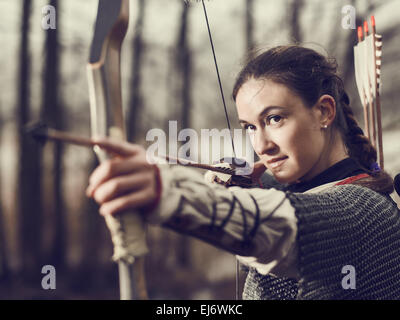 Archer médiéval femme, elle porte une maille et utiliser un arc et une flèche, forêt sombre, contre-image traitée. Banque D'Images