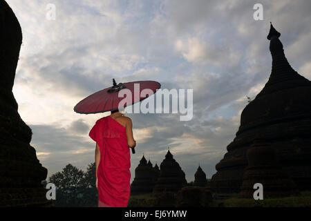 Monk holding parapluie rouge avec Andaw thein-Temple, Mrauk-U, l'État de Rakhine, au Myanmar Banque D'Images