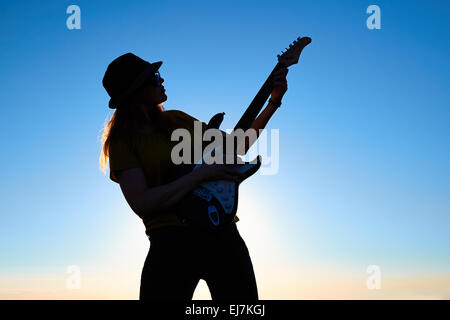 Silhouette de femme musicien ambulant en face de lever du soleil. Corps de femmes de flexion de la guitare sur maintien de musicien le soleil levant background Banque D'Images