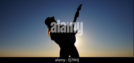 Silhouette de femme musicien ambulant en face de lever du soleil. Corps de femmes de flexion de la guitare sur maintien de musicien le soleil levant background Banque D'Images