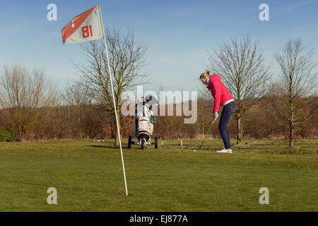 Golfeur femme jouant une partie de golf sous le soleil de fin de soirée de l'alignement sur le fairway pour un tir avec son chariot de golf Banque D'Images