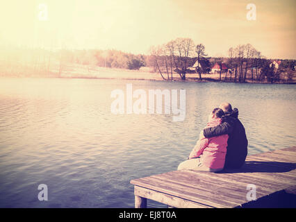 Retro photo filtrée d'un couple sitting on pier by lake. Banque D'Images