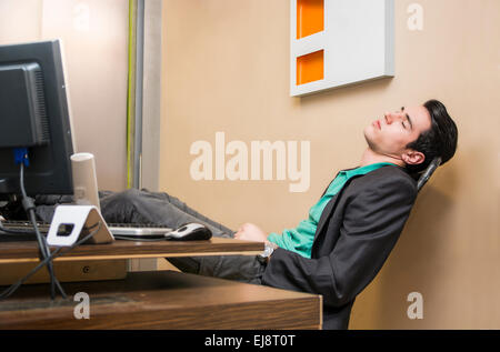 Surmené, fatigué young businessman sleeping à son bureau à l'office de tourisme, en face de l'ordinateur Banque D'Images