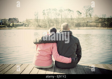 Sépia rétro photo stylisée d'un couple sitting on wooden pier par lac. Banque D'Images