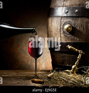 La nature morte avec verre de vin, la bouteille et le baril sur la table dans la cave. Banque D'Images