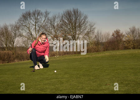 Golfeur féminin alignement d'un putt à genoux sur le green à la recherche au niveau du trou pour vérifier l'herbe et toute une pente de carrossage Banque D'Images