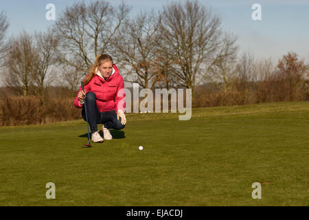 Golfeur féminin alignement d'un putt à genoux sur le green à la recherche au niveau du trou pour vérifier l'herbe et toute une pente de carrossage Banque D'Images