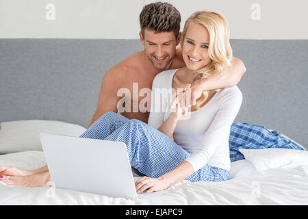 Young couple relaxing in bed using a laptop Banque D'Images