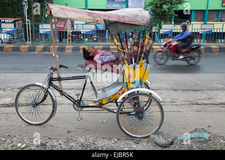 Rickshaw rider dort sur trike dans Silliguri Street, West Bengal, India Banque D'Images