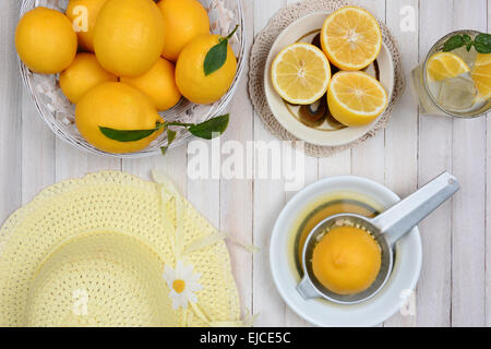 Rendre la vie encore limonade tourné d'un angle élevé sur une table de cuisine en bois blanc rustique, de citrons, centrifugeuse, bonnet jaune et g Banque D'Images