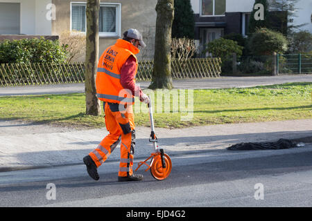 Un homme en vêtements fluorescents gigogne utilise une roue à mesurer une distance le long d'une route Banque D'Images