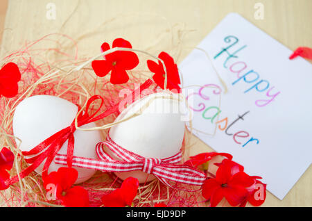 Deux œufs blancs dans un nid avec des fleurs et une carte "Joyeuses Pâques" Banque D'Images