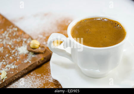 Tasse blanche avec plein de café délicieusement à la noix entière et le chocolat dans l'arrière-plan Banque D'Images