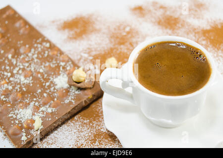 Tasse blanche avec plein de café délicieusement à la noix entière et le chocolat dans l'arrière-plan Banque D'Images