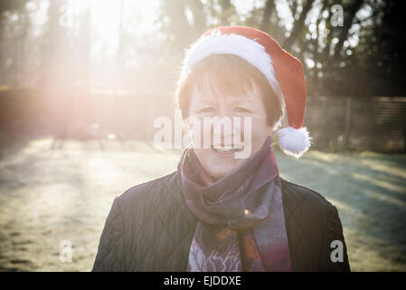 Une femme debout dans un jardin, portant un chapeau de Père Noël Noël. Banque D'Images