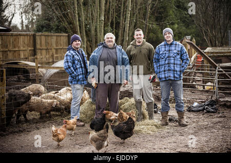 Quatre hommes, frères et un autre homme debout dans une ligne, dans une ferme à côté d'une plume pleine de jeunes porcs. Banque D'Images