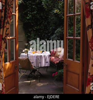 Vue à travers des portes de terrasse avec table pour petit déjeuner en petite ville jardin Banque D'Images