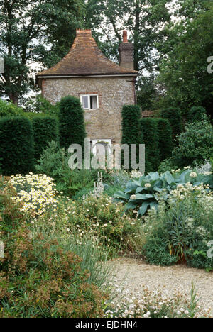 Crème haut de vivaces et clippé yew en grand pays jardin en été avec une brique +flint cottage dans l'arrière-plan Banque D'Images