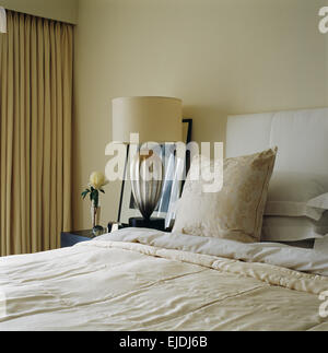 Lampe en verre à l'ombre en crème sur la table à côté de lit avec tête de lit rembourrée et coussin crème et couvre-lits en chambre à coucher moderne Banque D'Images