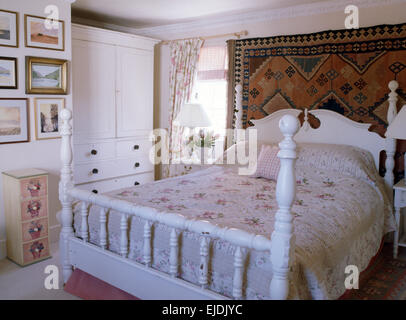 Accroché sur tapis mur à l'arrière en bois peint blanc à motifs rose lit avec couette bien en chambre cottage Banque D'Images