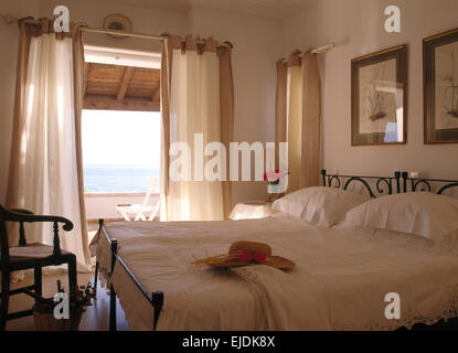 Le linge blanc sur des lits en fer forgé dans la région côtière de chambre avec des rideaux blancs sur les portes de balcon avec vue sur la mer Banque D'Images