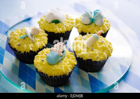 Cupcakes à thème Bébé garçon en bleu et jaune disposés sur un plateau en verre Banque D'Images