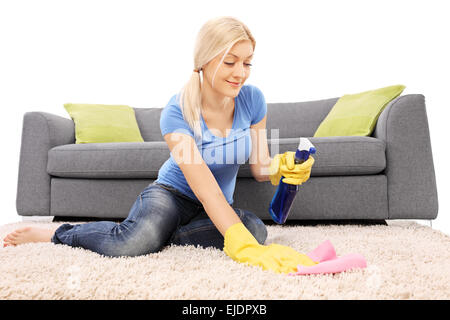 Le nettoyage du tapis femme avec un spray de nettoyage et le port de gants de protection jaune Banque D'Images