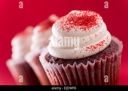 Trois délicieux petits gâteaux en velours rouge sur fond rouge. Banque D'Images