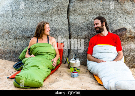Homme et une femme sur la plage dans des sacs de couchage laughing Banque D'Images