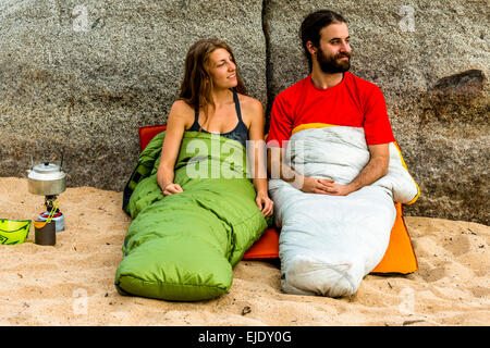 Homme et une femme sur la plage dans des sacs de couchage smiling Banque D'Images