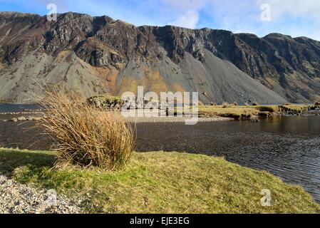 Wastwater pierriers sous le soleil d'hivers lumineux soirée avec ciel bleu et nuages blancs et de l'herbe et le lac au premier plan Banque D'Images