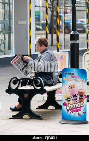 Femme assise sur un banc de lire le journal dans le centre-ville de Newton Abbot Banque D'Images